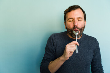 Gourmet man savoring food with spoon and closed eyes on blue background