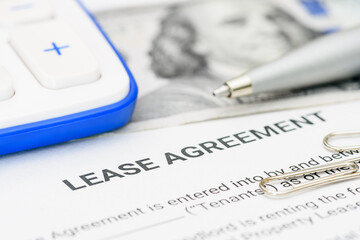 Lease agreement documentation and financial planning. A lease agreement, a calculator, pen, and paper clips, emphasizing financial calculations and legal preparations for rental or leasing contracts.