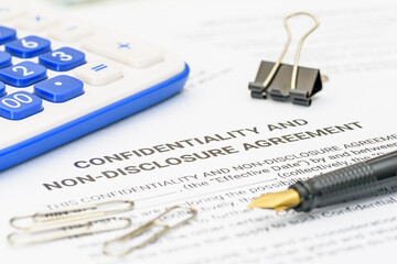 A close-up view of a confidentiality and non-disclosure agreement (NDA) document, with a calculator and a pen, symbolizing the importance of maintaining privacy and protecting sensitive information.
