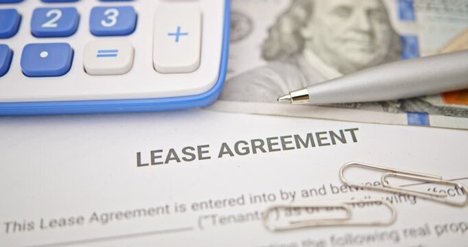 Lease agreement documentation and financial planning. A lease agreement, a calculator, pen, and paper clips, emphasizing financial calculations and legal preparations for rental or leasing contracts.