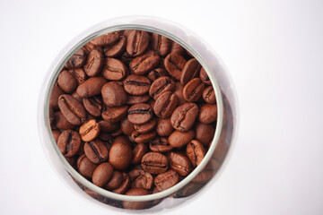 Fototapeta premium A detailed close-up of a glass filled with rich, roasted coffee beans set against a clean white background, showcasing the texture and quality of the beans, ideal for coffee lovers and gourmet