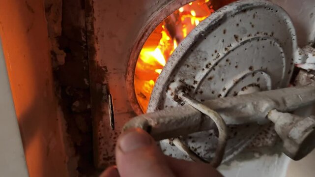Opening firebox door of masonry heater and burning firewood inside