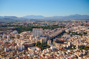 Obraz premium Vibrant aerial view captures sprawling city landscape with mountains in the background on a clear sunny day. Alicante, Spain 10.01.2023
