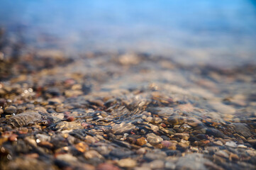 Clear water gently flows over smooth pebbles in a calm river setting during a sunny afternoon