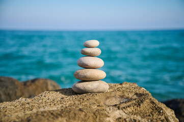 Balancing stones on a rock formation by the tranquil sea under a clear blue sky