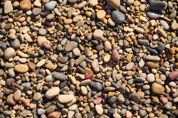 Colorful pebbles scattered across a sunlit sandy beach at midday