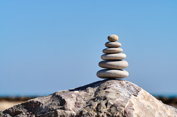Stones stacked harmoniously on a large rock against a clear blue sky at a serene beach location