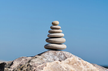 Stacked stones balanced on a large rock with a blue sky in the background during daylight hours