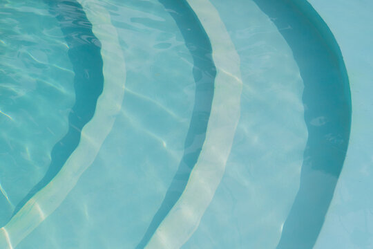 abstract background with crystal clear transparent blue water surface in swimming pool, ripples, sunlight and stair steps in summer sun