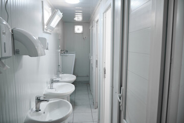 Public toilet container with washbowls, urinals and closed doors of toilet stalls. Toilet inside of prefabricated toilet container 