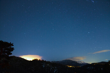 Fototapeta premium Starry Night Sky Over Mountain Landscape with Glowing Horizon and Snow-Capped Peaks