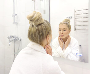 Obraz premium woman looking in the mirror in the bathroom and taking care of her skin.