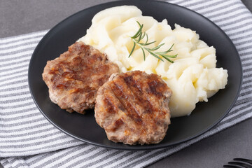 Savory grilled patties with creamy mashed potatoes and fresh rosemary on a dark plate