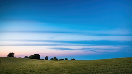 A serene twilight landscape featuring lush green fields under a vibrant blue sky with soft gradients of orange and pink as the sun sets.