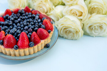 cake made from blueberries and strawberries and delicate white rose flowers on a light background. copy space 