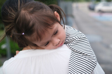 Obraz premium A tender moment capturing a child resting on a caretaker's shoulder, showcasing love, trust, and comfort, with a serene outdoor backdrop.