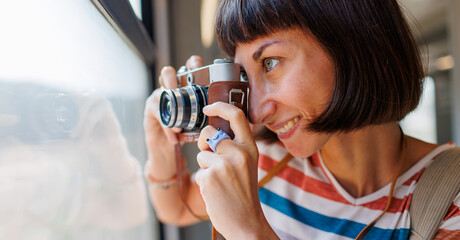 Fototapeta premium train travel. Young woman enjoying a train ride with a camera. tourist takes pictures of beautiful tourist places on camera. film camera.