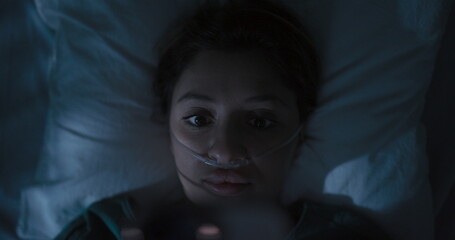 Tired female patient in hospital ward surfs Internet in the middle of the night.