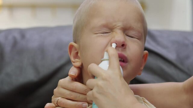 Mother using salt water nasal spray to rinse her child's nose. Irrigation of the nose with seawater.