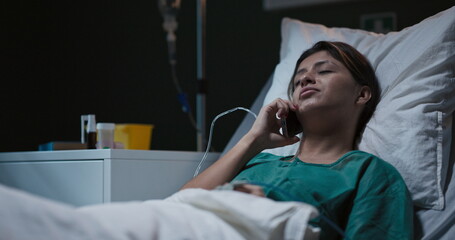 Hospitalized young woman chats on the phone from her bed in the ward.
