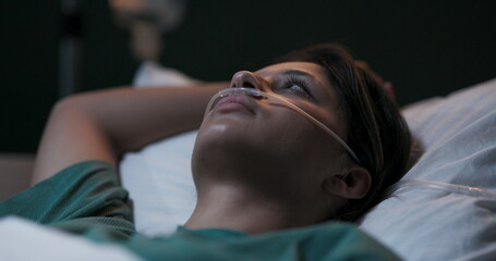 Woman in hospital ward receiving oxygen therapy through nasal tube.
