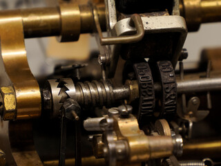 A detailed close-up shot reveals the intricate, brass and steel mechanisms of an antique printing press, emphasizing the texture and worn quality of the machine's components.