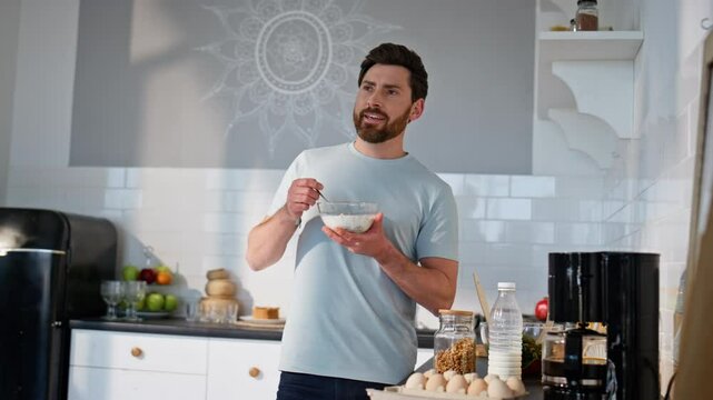 Satisfied man having breakfast at kitchen closeup. Smiling guy eating granola