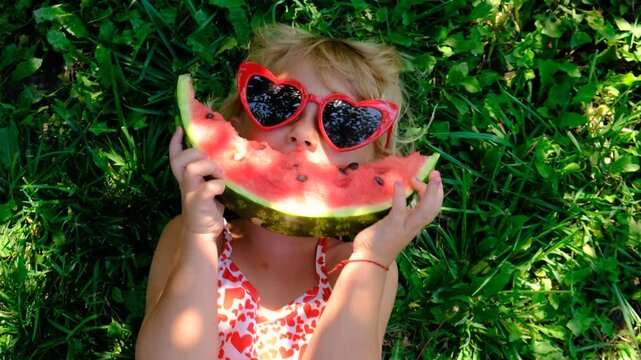Child in sunglasses eating watermelon in the garden. Selective focus.