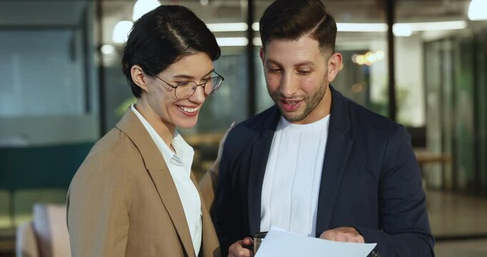 Two teammates discussing content of document during break in office, female holding mug explains important detail to colleague holds papers, smiling, reviewing successful results, revenue, get benefit