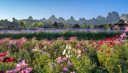 Obraz premium A vibrant landscape filled with colorful flowers, rolling hills, and quaint huts under a clear blue sky.