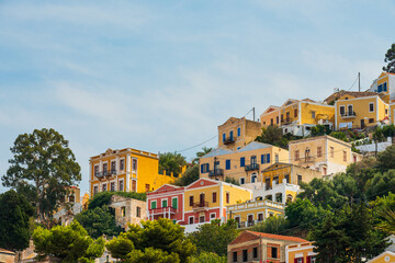 Obraz premium Scenic view of Symi island, Greece, with its traditional colorful houses and impressive monastery on the hillside. Calm sea and authentic architecture, an atmosphere of Mediterranean comfort.