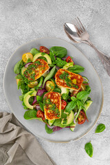 Salad with grilled halloumi cheese, tomatoes, avocado, cucumber and pesto sauce on a concrete background. Healthy food. Top view.
