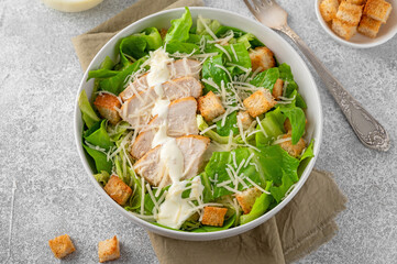 Caesar salad with lettuce, grilled chicken breast, parmesan cheese and croutons in a bowl on a gray concrete background. Copy space