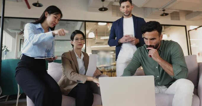 Four professionals taking part in briefing in co-working office using laptop, reviewing information related to task, engaged in brainstorming, project planning, collaborative problem-solving meeting