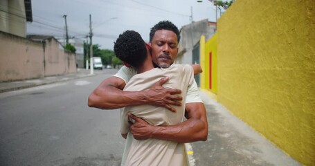 Father of African descent tightly embracing son in an urban street, a heartfelt moment symbolizing unconditional love, emotional support, and the strength of their bond