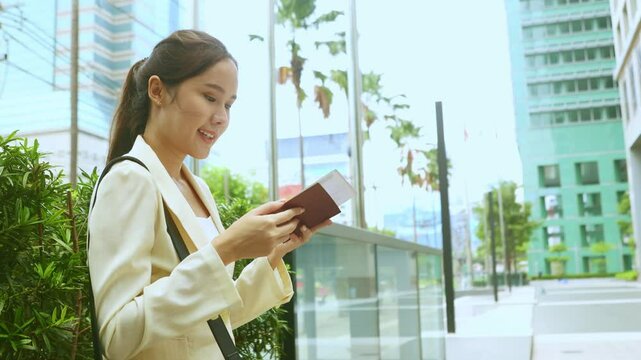 Asian female tourist checks passport validity in front of city office building and checks air ticket in preparation for travel.