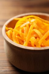 Fresh orange zest in bowl on wooden table, closeup