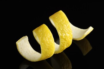 One curly lemon peel on black mirror surface, closeup