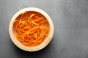 Fresh orange zest in bowl on grey textured table, top view. Space for text