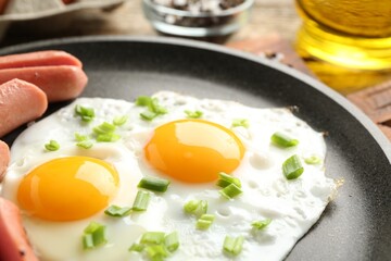 Tasty fried eggs with cut sausages and green onion in frying pan on table, closeup