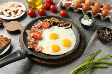 Tasty fried eggs with bacon and mushrooms served on grey table