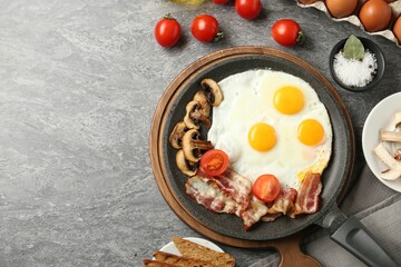 Tasty fried eggs with bacon and mushrooms served on grey table, flat lay. Space for text