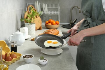 Woman putting tasty fried eggs onto plate from frying pan in kitchen, closeup