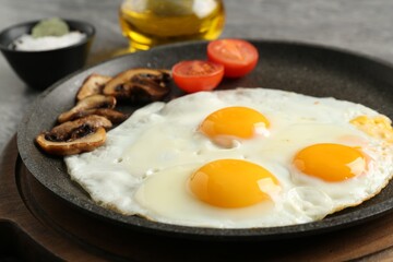 Tasty fried eggs with mushrooms and tomato in frying pan on table, closeup
