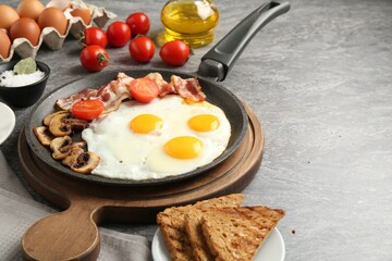 Tasty fried eggs with bacon and mushrooms served on grey table, closeup. Space for text