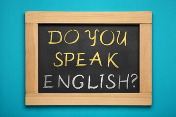 Obraz premium Small black chalkboard with text Do You Speak English? on blue wall. Language course