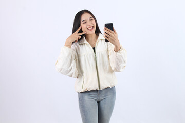 Fototapeta premium Smiling Adult Asian Woman Taking a Selfie in Casual Cream Jacket and Jeans