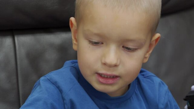 Child playing with new toy sitting on sofa at home. Concentrated face of little boy holding transformer robot toy. Three year old child examining new toy comments on his actions.