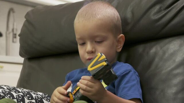 Child playing with new toy sitting on sofa at home. Concentrated face of little boy holding transformer robot toy. Three year old child examining new toy comments on his actions.