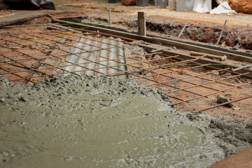 Wet concrete poured over reinforced steel mesh at a construction site. Wet concrete for residential floor construction